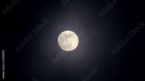 Full moon on dark cloudy night. Clouds passing by the moon, real time shot.