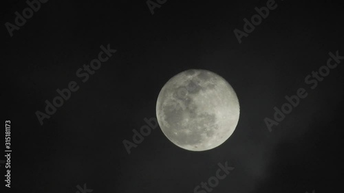 Full moon on dark cloudy night. Clouds passing by the moon, real time shot.