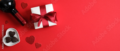 Valentine's day banner template with wine bottle, valentine gift, heart shaped candies on red background with copy space. Top view, flat lay. Romantic dinner couple concept