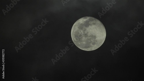 Full moon on dark cloudy night. Clouds passing by the moon, real time shot.