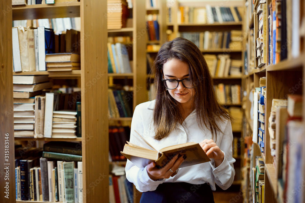 Female student in library reading a book, looking for materials to make research Female student in library reading a book, looking for materials to make research