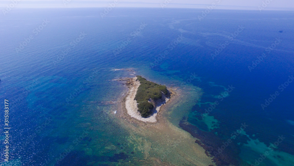 Small island with green trees and rocky coast in the blue sea. Aerial view 