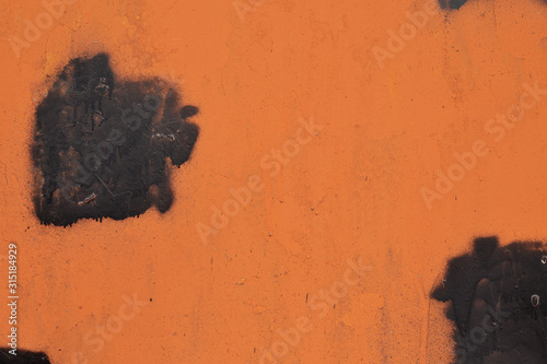 texture of an orange metal wall with black large stain on it