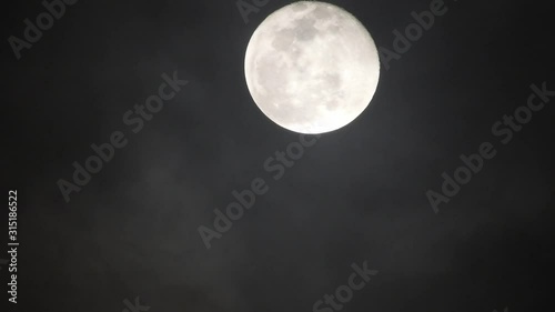 Full moon on dark cloudy night. Clouds passing by the moon, real time shot.