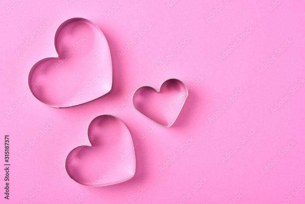 Valentines Day Concept: Three Heart shaped cookie cutters on pink  with copy space.