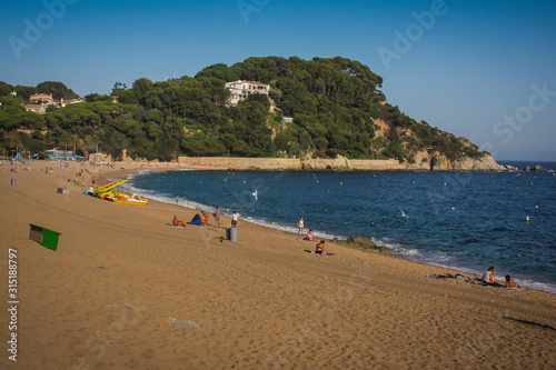 Fenals beach in Lloret de Mar area in Spain. Late clear afternoon setting on a beach with blue ocean water on the mediterranean. Some people are seen on the beach.