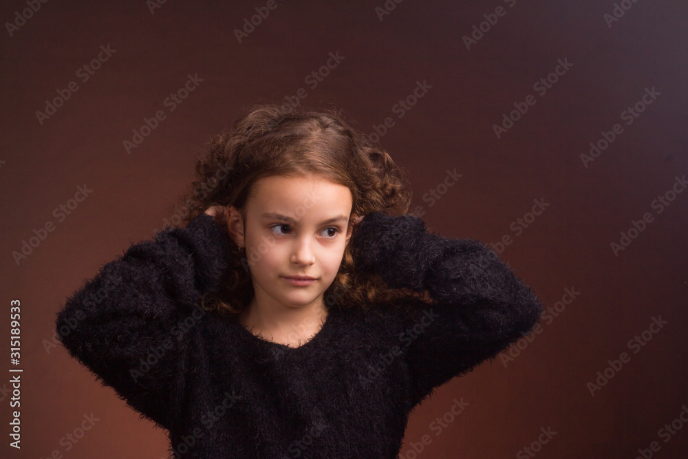 Studio portrait of little girl with long curly hair in a black fluffy jacket and a pink skirt