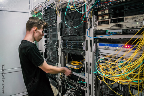 A young guy connects a wire to a switch in a server room. Information Technology Concept. The specialist works in a data center.
