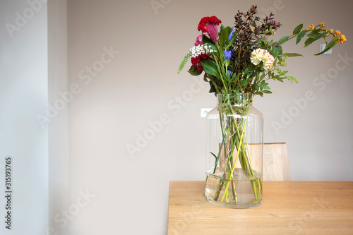 Fresh bright colorful bouquet of flowers in glass vase on the wooden table in a light room