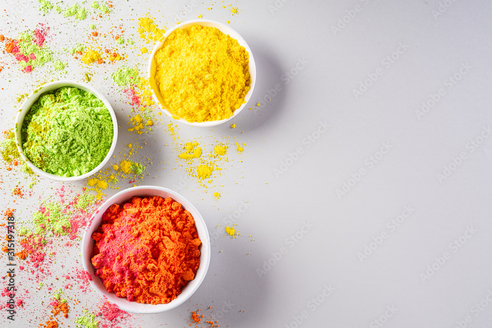 Holi festival celebration. Traditional Indian Holi colours powder decoration with paints. Top view of Organic Gulal colors in bowls on gray background for Holi festival. Holi festival celebration. Traditional Indian Holi colours powder decoration with paints. Top view of Organic Gulal colors in bowls on gray background for Holi festival.