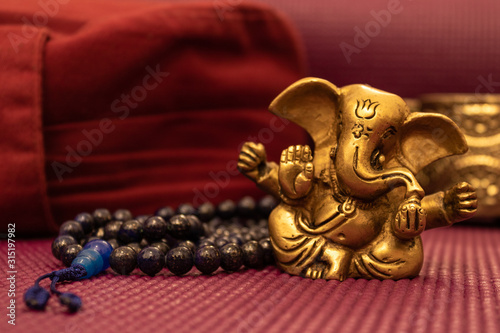 Golden statue of ganesha on yoga mat with blue prayer beads and yoga pillow. Meditation background.