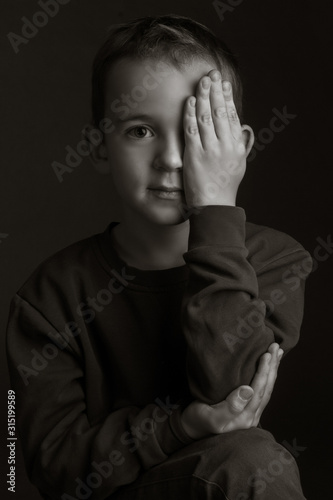 black-white portrait of a dark-haired boy covering his eye with his hand on a black background