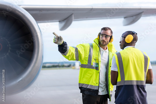 Air traffic control ground crew workers talking near airplane on airport tarmac photo