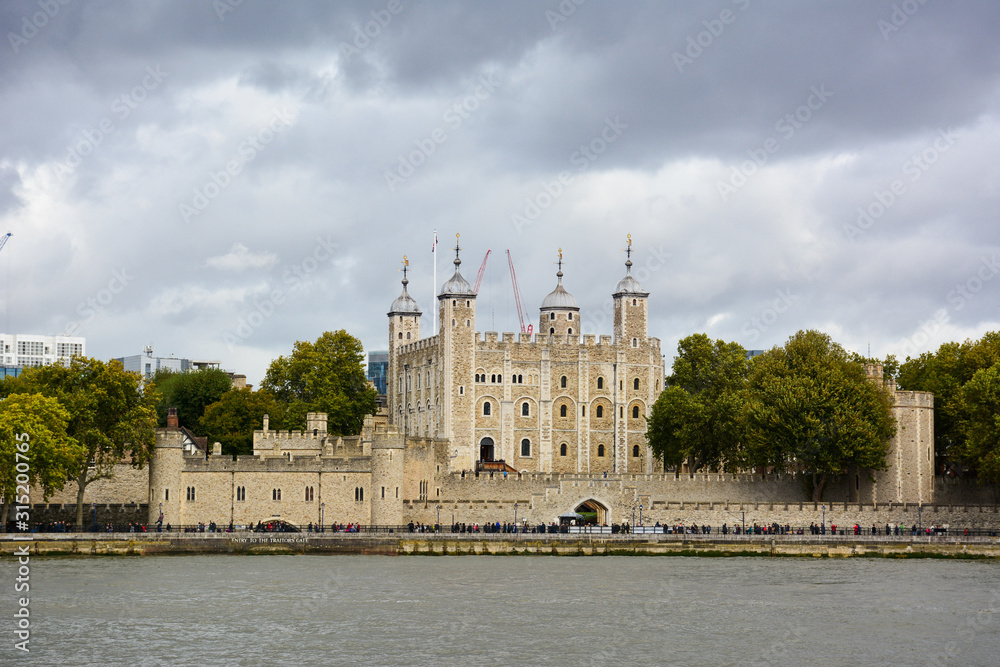Fototapeta premium Tower of London, a castle and a former prison in London, England, seen from the River Thames on a cloudy day. Museum collections include famous British crown jewels