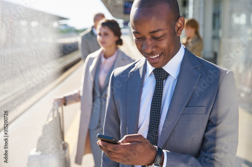 Businessman texting with cell phone on train station platform photo