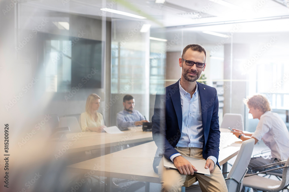 Portrait businessman holding laptop in conference room