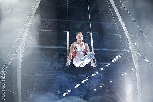 Focused male gymnast performing on gymnastics rings in arena