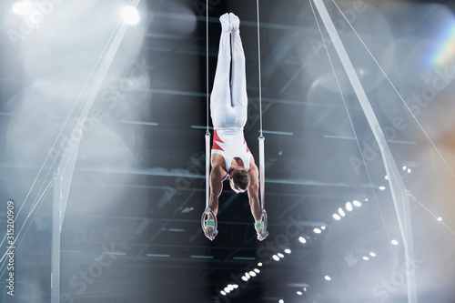 Male gymnast performing upside-down on gymnastics rings in arena