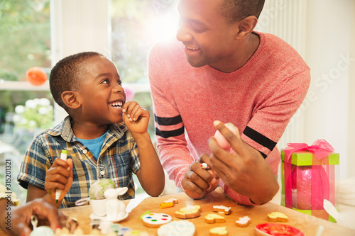 Smiling father and son decorating Easter eggs and cookies photo