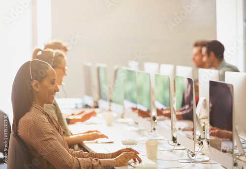 Telemarketers wearing headsets working at computers in a row in sunny office photo