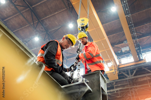Steel workers fastening steel to crane in factory photo