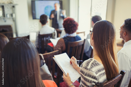Businesswoman in audience taking notes at business conference