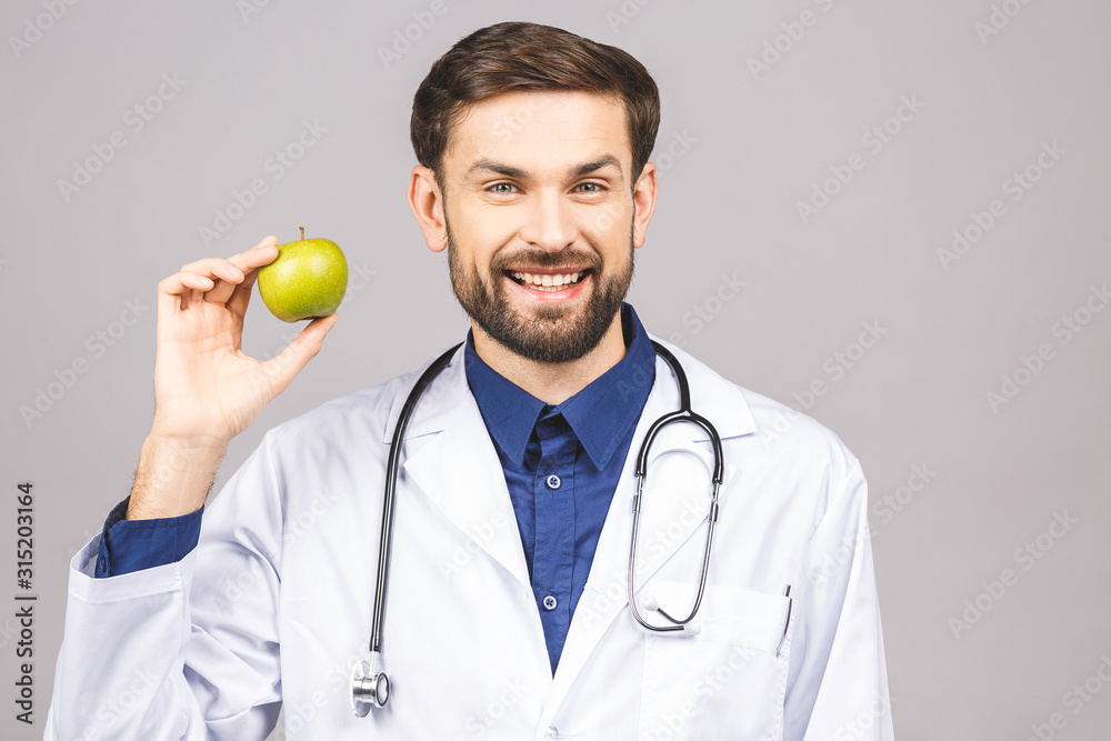 Doctor giving apple concept for healthy eating and lifestyle or good diet. A male medical doctor with stethoscope holding a green apple isolated on grey background.