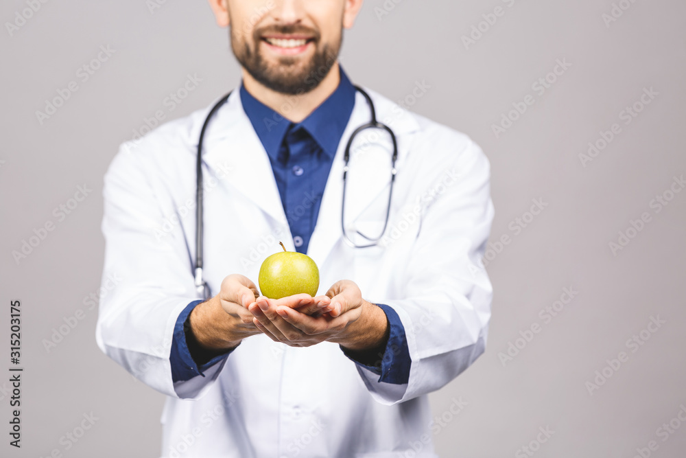 Doctor giving apple concept for healthy eating and lifestyle or good diet. A male medical doctor with stethoscope holding a green apple isolated on grey background. Doctor giving apple concept for healthy eating and lifestyle or good diet. A male medical doctor with stethoscope holding a green apple isolated on grey background.