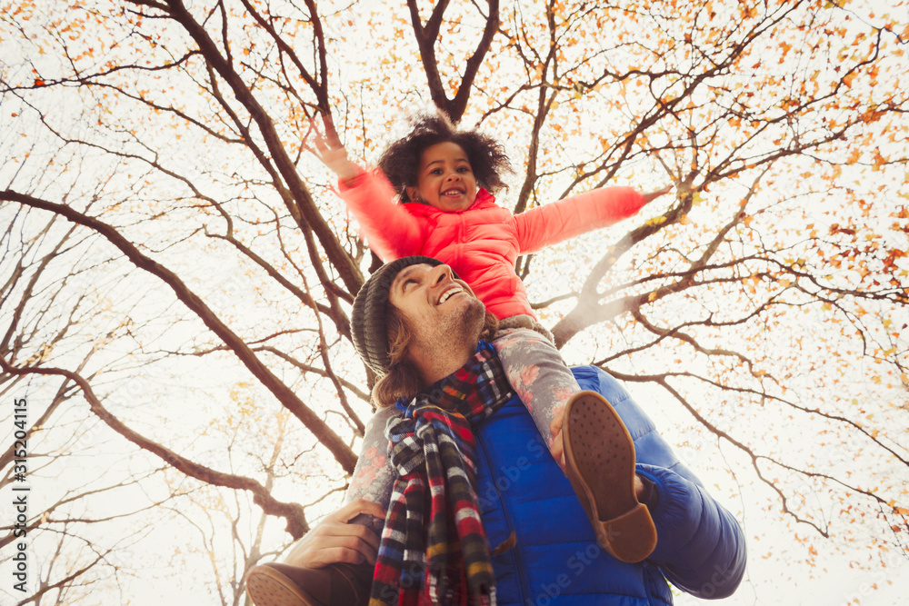 Father carrying daughter on shoulders under tree in autumn park Father carrying daughter on shoulders under tree in autumn park