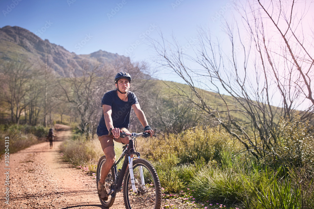 Young man mountain biking on sunny, remote dirt road Young man mountain biking on sunny, remote dirt road