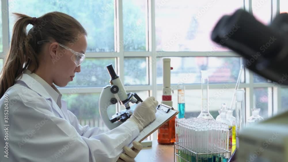 zoom in video shot of Young female scientists took a test tube to analyze and use a pen to record the results on paper. zoom in video shot of Young female scientists took a test tube to analyze and use a pen to record the results on paper.