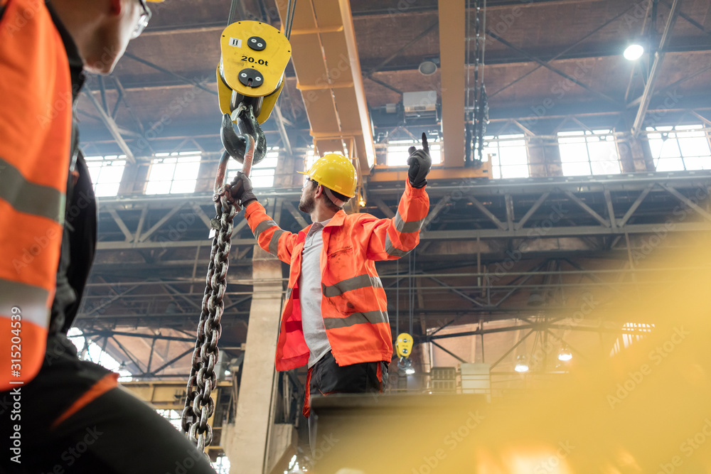 Steel workers fastening chain to crane in factory Steel workers fastening chain to crane in factory
