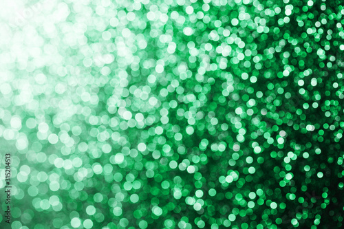 Green bokeh shiny glitter background. Vibrant color glowing spots texture for graphic design.