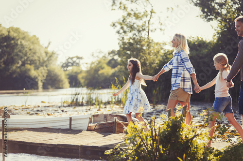 Family holding hands and walking on sunny lakeside dock photo