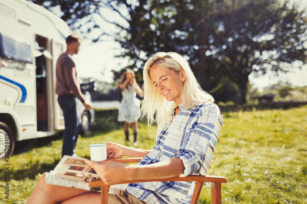 Woman reading magazine and drinking coffee outside sunny motor home Woman reading magazine and drinking coffee outside sunny motor home