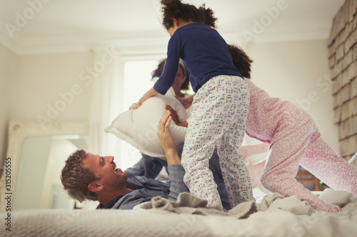 Playful multi-ethic father and daughters pillow fighting on bed photo