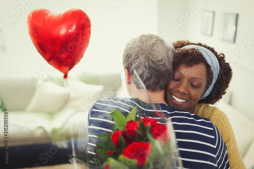 Wife hugging husband giving Valentine‚Äôs Day balloon and rose bouquet photo