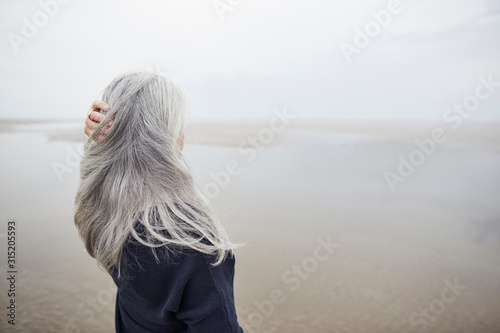 Senior woman with hand in long gray hair on winter beach photo