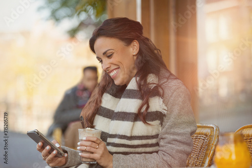 Smiling woman texting cell phone drinking milkshake at sidewalk cafe photo