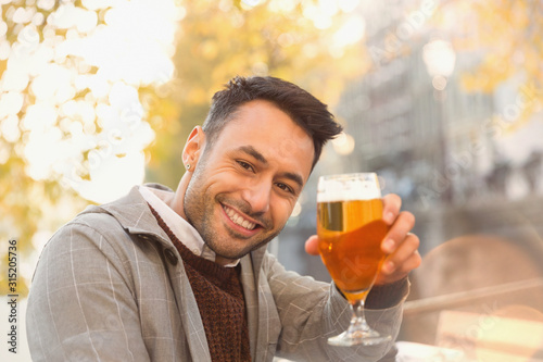 Portrait smiling young man drinking beer at autumn sidewalk cafe photo