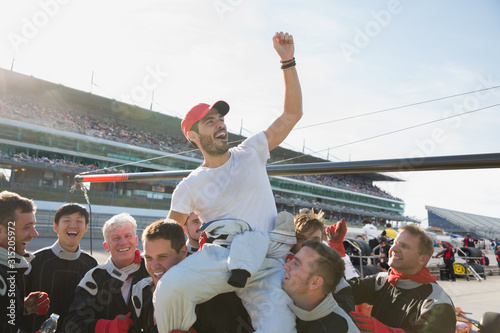Formula one racing team carrying cheering driver on shoulders, celebrating victory on sports track