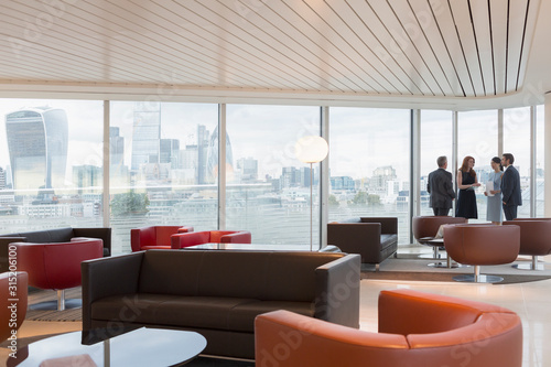 Business people talking at window in urban highrise office lounge city view photo