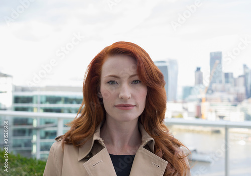 Portrait serious, confident businesswoman red hair on urban balcony city view photo