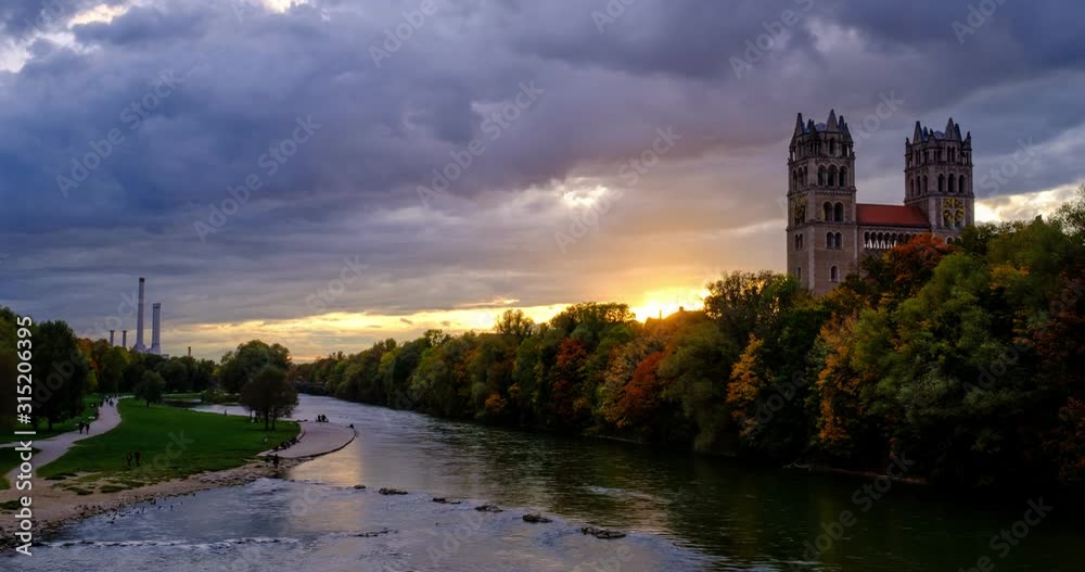 Timelapse of Munich at dramatic sunset: autumn in park of famous tourist landmark Bavarian city. View of Isar river, trees, church. Munchen, Bavaria, Germany. Camera zoom in