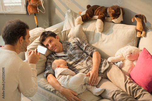 Male gay parents and baby son resting on living room sofa photo