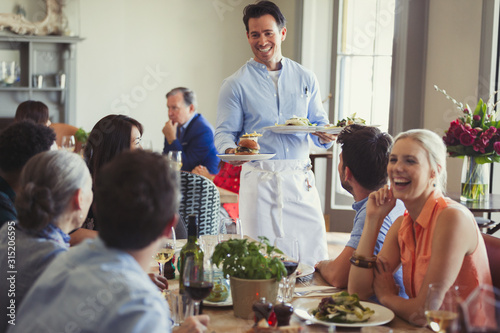 Smiling waiter serving food to friends dining at restaurant table