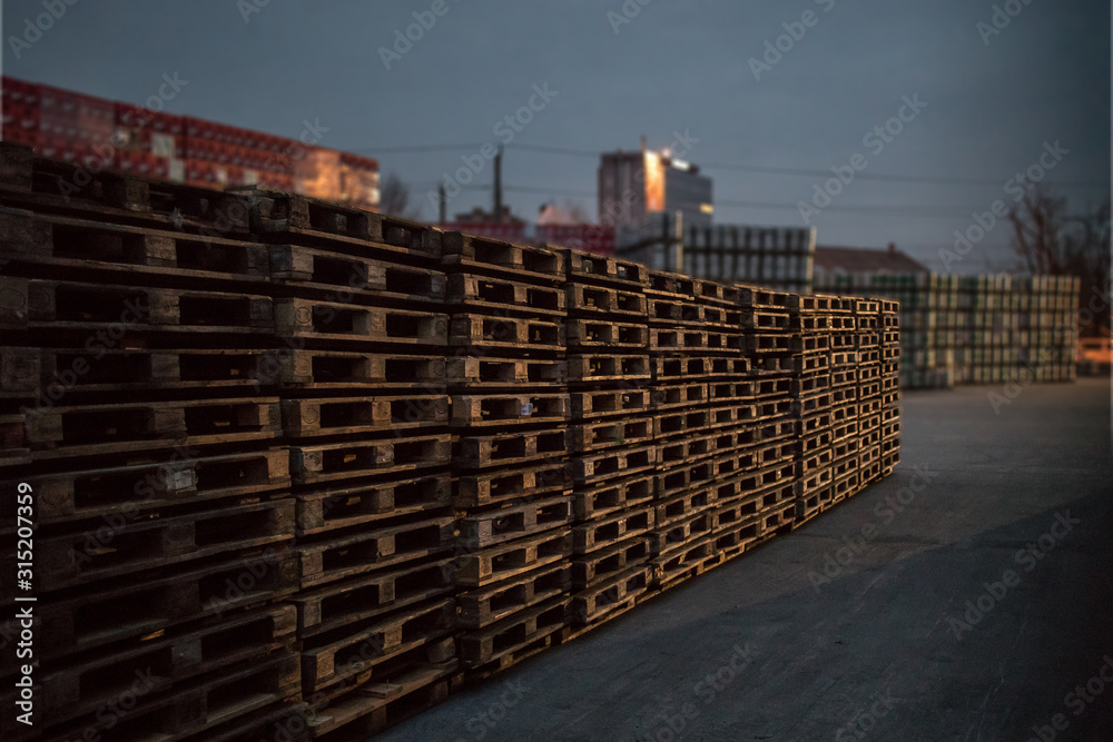 A row or stack of wooden euro palettes in early foggy morning. Used euro palettes waiting in an open space warehouse during early morning hours. A row or stack of wooden euro palettes in early foggy morning. Used euro palettes waiting in an open space warehouse during early morning hours.