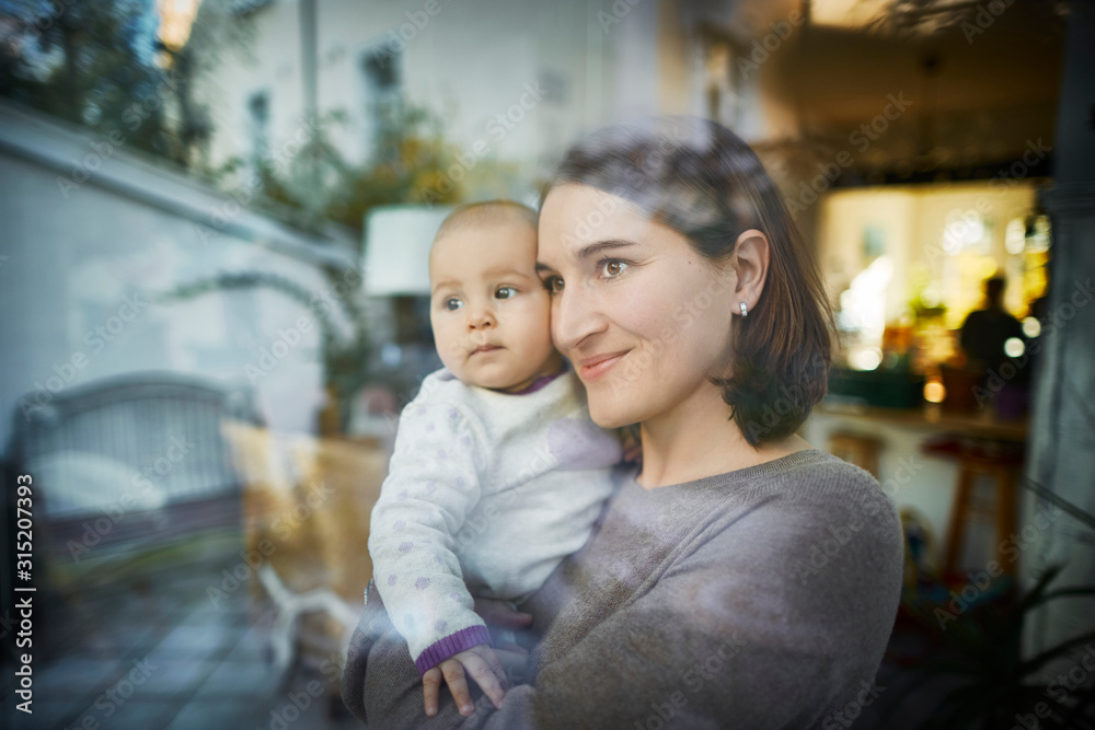 Smiling mother holding baby daughter at window Smiling mother holding baby daughter at window