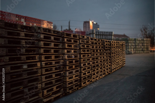 A row or stack of wooden euro palettes in early foggy morning. Used euro palettes waiting in an open space warehouse during early morning hours.