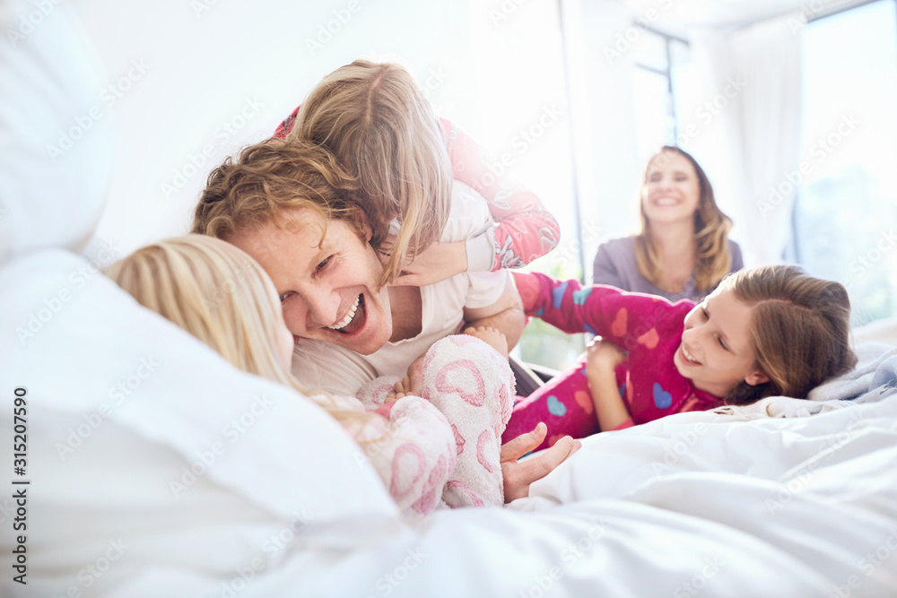 Playful father and daughters tickling on bed Playful father and daughters tickling on bed